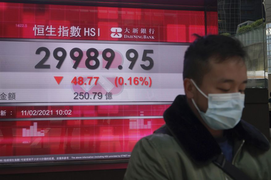 A man wearing a face mask walks past a bank's electronic board showing the Hong Kong share index in Hong Kong, Thursday, Feb. 11, 2021. Despite a short drop in early trading in Hong Kong, most major Asian stock indexes were higher on Thursday after President Joe Biden held his first conversation with Chinese leader Xi Jinping since taking office. (AP Photo/Kin Cheung)