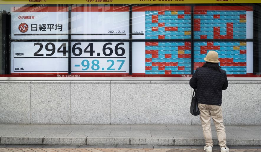 A man looks at screens showing Japan's Nikkei 225 index and companies' stock prices at a securities firm in Tokyo on Friday, Feb. 12, 2021. Shares fell in Tokyo and Sydney on Friday after stocks closed nearly flat on Wall Street, while most Asian markets were closed to mark the Lunar New Year. (AP Photo/Hiro Komae)