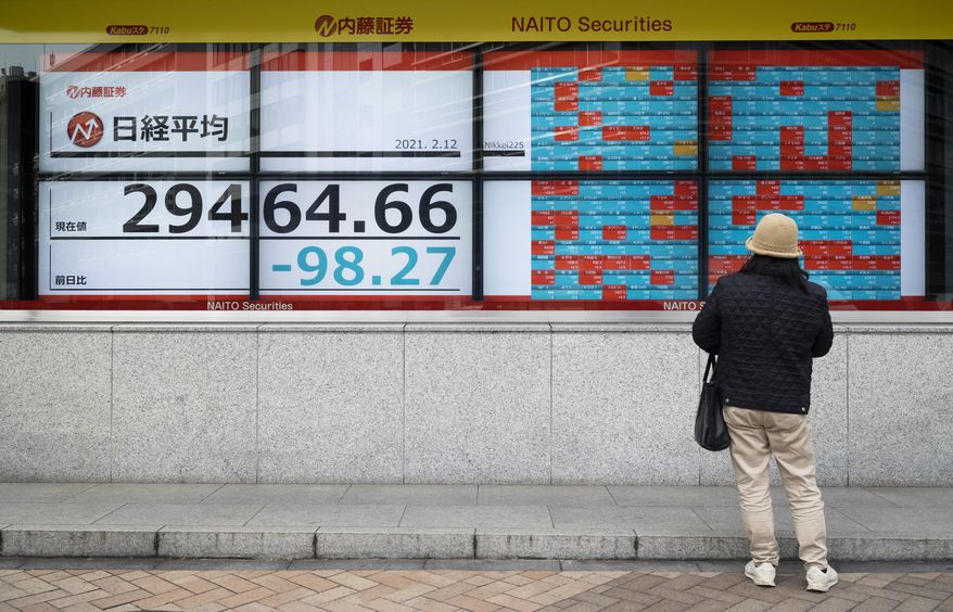 A man looks at screens showing Japan's Nikkei 225 index and companies' stock prices at a securities firm in Tokyo on Friday, Feb. 12, 2021. Shares fell in Tokyo and Sydney on Friday after stocks closed nearly flat on Wall Street, while most Asian markets were closed to mark the Lunar New Year. (AP Photo/Hiro Komae)