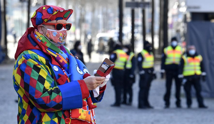 A carnival reveler is watched by public order guards at the &amp;quot;Alter Markt&amp;quot; where normally tens of thousands of revelers dressed in carnival costumes would celebrate the start of the street carnival in Cologne, Germany, Thursday, Feb. 11, 2021. This year all carnival celebrations are banned due to the coronavirus pandemic. (AP Photo/Martin Meissner)
