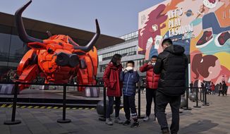 A man and a child put on their face mask to help curb the spread of the coronavirus after taken a souvenir photo near a Year of the Ox statue on display at the capital city&#39;s popular shopping mall during the first day of the Lunar New Year in Beijing, Friday, Feb. 12, 2021. Festivities for the holiday, normally East Asia&#39;s busiest tourism season, are muted after China, Vietnam, Taiwan and other governments tightened travel curbs and urged the public to avoid big gatherings following renewed virus outbreaks. (AP Photo/Andy Wong)