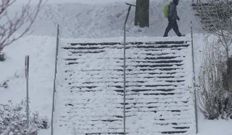 A pedestrian walks near a snow-covered staircase, Saturday, Feb. 13, 2021, on the University of Washington campus in Seattle. Winter weather was expected to continue through the weekend in the region.(AP Photo/Ted S. Warren)