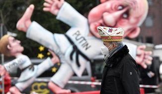 A reveller stands in front of a political carnival float depicting Russia&#39;s President Vladimir Putin fighting with opposition leader Alexei Navalny in the streets of Duesseldorf, Germany, Monday, Feb. 15, 2021. Because of the coronavirus pandemic the traditional &#39;Rosenmontag&#39; carnival parade are canceled but eight floats are pulled through the empty streets in Duesseldorf, where normally hundreds of thousands of people would celebrate the street carnival. (AP Photo/Martin Meissner)