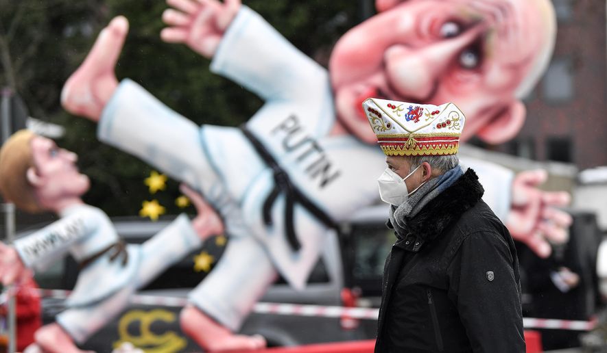 A reveller stands in front of a political carnival float depicting Russia&#x27;s President Vladimir Putin fighting with opposition leader Alexei Navalny in the streets of Duesseldorf, Germany, Monday, Feb. 15, 2021. Because of the coronavirus pandemic the traditional &#x27;Rosenmontag&#x27; carnival parade are canceled but eight floats are pulled through the empty streets in Duesseldorf, where normally hundreds of thousands of people would celebrate the street carnival. (AP Photo/Martin Meissner)