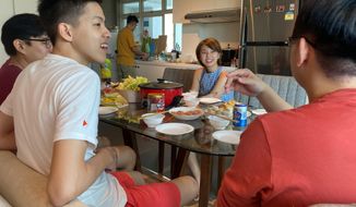 Chan Jit Yen smiles as she hosts Malaysian students, foreground, during a Lunar New Year hot pot lunch at her rented apartment in Singapore Saturday, Feb. 13, 2021. With Malaysian workers and students stranded in the city state over the Lunar New Year due to coronavirus travel restrictions, the Malaysian Association in Singapore has called on Malaysians to treat students to a meal. (AP Photo/Annabelle Liang)
