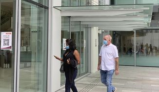 Agatha Maghesh Eyamalai, left, and Skea Nigel walk into the State Courts in Singapore, Monday, Feb. 15, 2021. The Briton man pleaded guilty on Monday to violating a coronavirus quarantine order in Singapore to visit his fiancee. (AP Photo/Annabelle Liang)