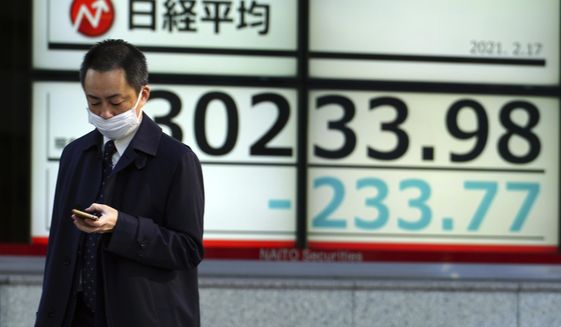 A man wearing a protective mask walks in front of an electronic stock board showing Japan&#39;s Nikkei 225 index at a securities firm Wednesday, Feb. 17, 2021, in Tokyo. Asian shares were lower Wednesday as investors sold to lock in profits from the recent rally driven by hopes economies will gradually return to a pre-pandemic normal. (AP Photo/Eugene Hoshiko)