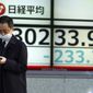A man wearing a protective mask walks in front of an electronic stock board showing Japan&#39;s Nikkei 225 index at a securities firm Wednesday, Feb. 17, 2021, in Tokyo. Asian shares were lower Wednesday as investors sold to lock in profits from the recent rally driven by hopes economies will gradually return to a pre-pandemic normal. (AP Photo/Eugene Hoshiko)