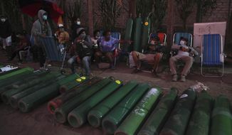 People sit next to their oxygen tanks as they prepare to spend the night waiting for a refill at a shop that has already closed for the day in Villa El Salvador, in Lima, Peru, Monday, Feb. 15, 2021, amid the COVID-19 pandemic. Some of the people in line said they have been waiting for two days for refills and are now staying for a third day to procure oxygen for sick relatives. (AP Photo/Martin Mejia)
