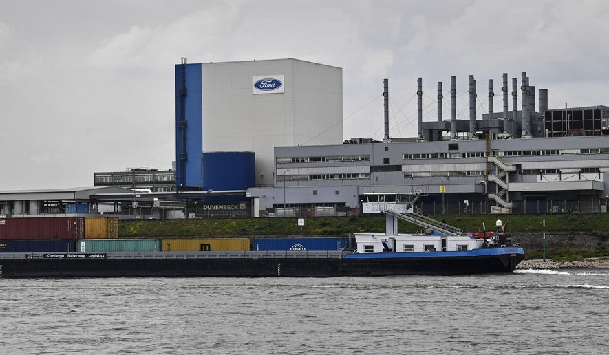 FILE - In this May 4, 2020 file photo, a container ship passes the Ford car plant in Cologne, Germany, as the US car maker restarts the production after the coronavirus lockdown. Ford says it will spend $1 billion to modernize its Cologne, Germany, manufacturing center, converting it into a European electric vehicle factory. (AP Photo/Martin Meissner)