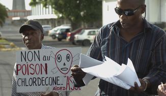 In this Nov. 18, 2007 photo, lawyer Harry Durimel, right, stands next to an activist with a sign that reads in French &amp;quot;No to Chlordecone poison,&amp;quot; as they protest during the arrival of the French government’s Health Minister Roselyne Bachelot in Raizet Abymes, Guadeloupe. Durimel is among the attorneys representing agricultural workers in Guadeloupe and Martinique who have long been fighting for compensation for the use of a banned pesticide, chlordecone. (AP Photo/Dominique Chomereau-Lamotte)