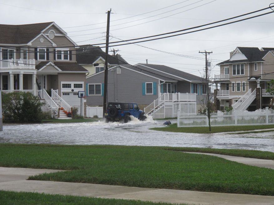 A vehicle kicks up a wake as it drives through a flooded street in Ocean City, N.J. on Oct. 30, 2020. The city is dealing with the costs of rising sea levels, both in monetary terms and in the disruption that recurring flooding brings. (AP Photo/Wayne Parry)