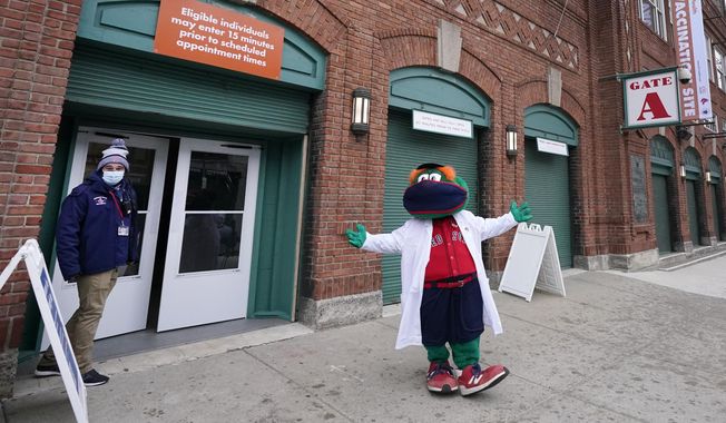 Boston Red Sox mascot, Wally the Green Monster, gestures while dressed in a medical white coat outside Fenway Park, Monday Feb. 1, 2021, in Boston. Fenway Park is one of several large COVID-19 vaccination sites in the Boston area. (AP Photo/Elise Amendola)
