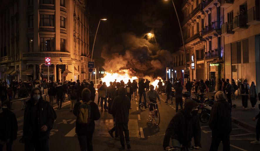 People gather next to a burning barricade during clashes after a protest condemning the arrest of rap singer Pablo Hasél in Barcelona, Spain, Wednesday, Feb. 17, 2021. Police fired rubber bullets and baton-charged protesters as clashes erupted for a second night in a row Wednesday at demonstrations over the arrest of Spanish rap artist Pablo Hasél. Many protesters threw objects at police and used rubbish containers and overturned motorbikes to block streets in both Madrid and Barcelona. (AP Photo/Felipe Dana)