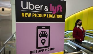 A passer-by walks past a sign offering directions to an Uber and Lyft ride pickup location at Logan International Airport, in Boston, Tuesday, Feb. 9, 2021. Uber and Lyft are taking different routes around the roadblock the virus pandemic dropped on their paths to profitability. The companies have racked up tens of billions of dollars in losses since starting up, and the slump in passenger activity has pushed profitability ever further off into the future.  (AP Photo/Steven Senne)