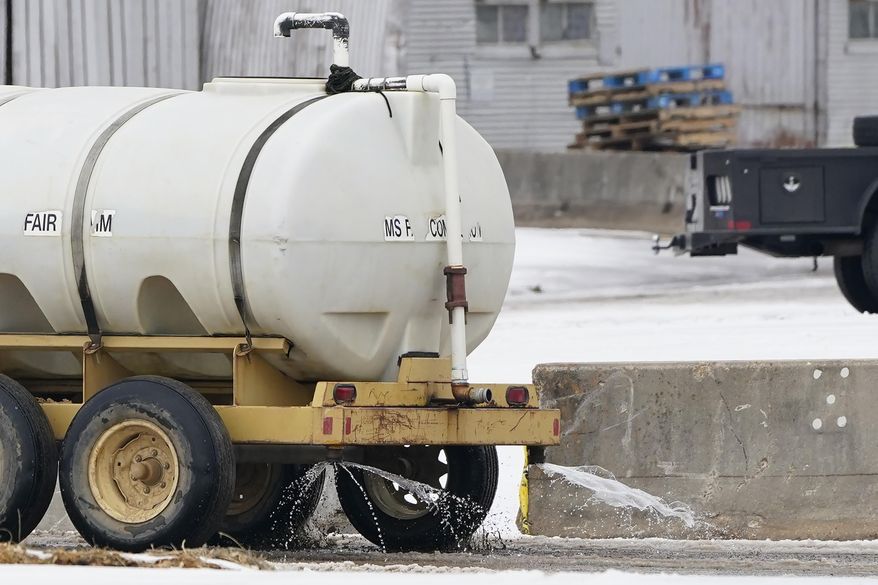A grounds keeper hauls a water tank sprinkler across the lanes at the Mississippi State Fairgrounds, to keep the dirt from dusting up Wednesday, Feb. 17, 2021, in Jackson, Miss., as light snow mixed with sleet, and rain continue to cover much of the state. In spite of the inclement weather, Wednesday's performance of the Dixie National Rodeo is taking place as scheduled. The National Weather Service in Jackson has issued a winter storm warning for parts of Mississippi ahead of another storm system set to impact the region. (AP Photo/Rogelio V. Solis)