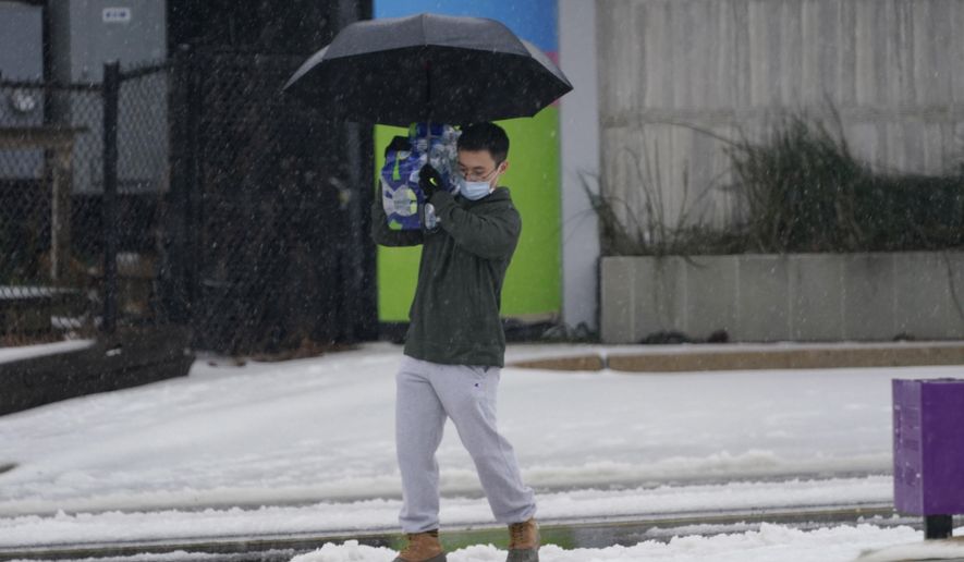 Panny Yang carefully treads this way across an ice strewn parking lot as he balances a 24-bottle pack of water on his shoulder, Wednesday, Feb. 17, 2021, in Jackson, Miss., as light snow mixed with sleet, and rain continue to cover much of the state. Areas of his neighborhood are without water as the city tries to handle a number of infrastructure issues. The National Weather Service in Jackson has issued a winter storm warning for parts of Mississippi as another storm system is set to impact the region. (AP Photo/Rogelio V. Solis)