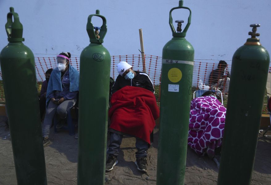 People sleep framed by their empty oxygen cylinders waiting for a shop to open to refill their tanks, in the Villa El Salvador neighborhood of Lima, early Thursday morning, Feb. 18, 2021, as the lack of medical oxygen to treat COVID-19 patients continues to be the norm in Peru. Long lines form outside private providers with many spending the night outside so as to not lose their place in line. (AP Photo/Martin Mejia)