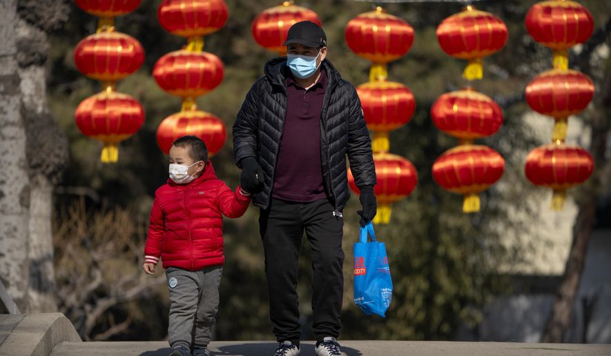 A man and child wearing face masks to protect against the spread of the coronavirus walk past lanterns at a public park in Beijing, Friday, Feb. 19, 2021. China appears to be considering further measures to lift its flagging birthrate, more than four years after ending the controversial one-child policy. (AP Photo/Mark Schiefelbein)