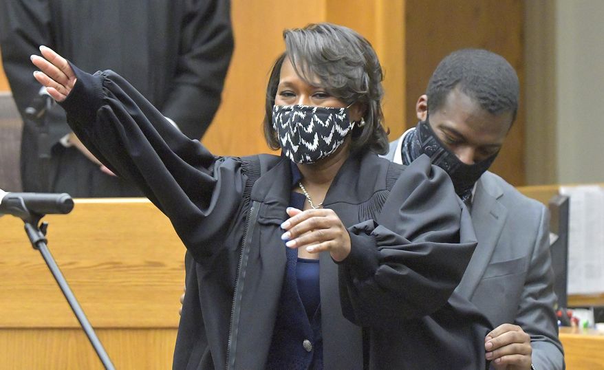 Ryan Barnes, right, places a judicial robe on his mother, Carla Barnes, as she was sworn onto the bench in the 11th Circuit Court at the Law and Justice Center in Bloomington, Ill., Thursday, Feb. 11. 2021. Barnes, who is the chief public defender in the county, becomes the first black judge in McLean County history. (David Proeber /The Pantagraph via AP)