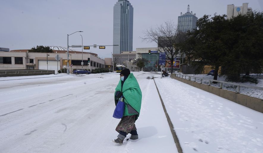 FILE - In this Feb. 16, 2021, file photo, a woman wrapped in a blanket crosses the street near downtown Dallas. As temperatures plunged and snow and ice whipped the state, much of Texas&#x27; power grid collapsed, followed by its water systems. Tens of millions huddled in frigid homes that slowly grew colder or fled for safety. (AP Photo/LM Otero, File)