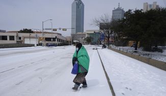 FILE - In this Feb. 16, 2021, file photo, a woman wrapped in a blanket crosses the street near downtown Dallas. As temperatures plunged and snow and ice whipped the state, much of Texas&#39; power grid collapsed, followed by its water systems. Tens of millions huddled in frigid homes that slowly grew colder or fled for safety. (AP Photo/LM Otero, File)