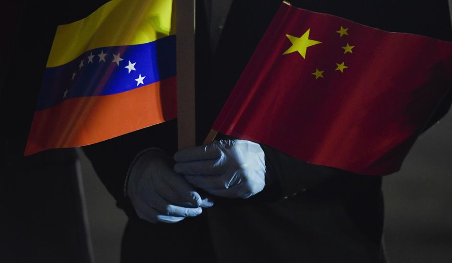 FILE - In this March 30, 2020 file photo, Venezuela's Foreign Minister Jorge Arreaza, wearing protective gloves as a preventive measure against the spread of the new coronavirus, holds a Venezuelan and Chinese flag as medical specialists and supplies arrive from China at the Simon Bolivar International Airport in La Guaira, Venezuela. While the pandemic has opened the door to much-welcomed Chinese aid in Latin America and Caribbean, it’s also made it harder for governments to pay their bills to Beijing, due to a deep recession last year wiped out nearly a decade’s worth of growth, according to International Monetary Fund data. (AP Photo/Matias Delacroix, File)