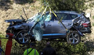 Workers watch as a crane is used to lift a vehicle following a rollover accident involving golfer Tiger Woods, Tuesday, Feb. 23, 2021, in the Rancho Palos Verdes section of Los Angeles. Woods suffered leg injuries in the one-car accident and was undergoing surgery, authorities and his manager said. (AP Photo/Ringo H.W. Chiu)