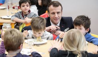 FILE - In this Jan.18, 2019 file photo, French President Emmanuel Macron meets pupils as he visits a school canteen in Saint-Sozy, southwestern France. By taking meat off the menu at school canteens, the Green Party mayor of Lyon has kicked up a storm of protest and debate in a country increasingly asking questions about the environmental costs of its meaty dietary habits. With a meatless four-course meal that Lyon City Hall says will be quicker and easier to serve to children who must be kept socially distanced while eating lunch to avoid coronavirus infections. (Ludovic Marin/Pool Photo via AP, FILE)