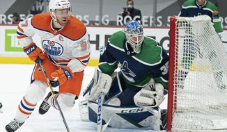 Edmonton Oilers center Connor McDavid (97) and Vancouver Canucks goaltender Thatcher Demko (35) look for the puck during the third period of an NHL hockey game Tuesday, Feb. 23, 2021, in Vancouver, British Columbia. (Jonathan Hayward/The Canadian Press via AP)