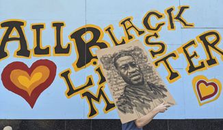 A demonstrator carries an image of George Floyd in front of a boarded up business decorated with a mural reading &quot;All Black Lives Matter,&quot; on Hollywood Boulevard, during a march organized by black members of the LGBTQ community in the Hollywood section of Los Angeles. The Black Lives Matter Global Network Foundation, which grew out of the creation of the Black Lives Matter movement, is formally expanding a $3 million financial relief fund that it quietly launched in February 2021, to help people struggling to make ends meet during the ongoing coronavirus pandemic. (AP Photo/Damian Dovarganes, File)