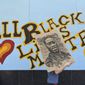 A demonstrator carries an image of George Floyd in front of a boarded up business decorated with a mural reading &quot;All Black Lives Matter,&quot; on Hollywood Boulevard, during a march organized by black members of the LGBTQ community in the Hollywood section of Los Angeles. The Black Lives Matter Global Network Foundation, which grew out of the creation of the Black Lives Matter movement, is formally expanding a $3 million financial relief fund that it quietly launched in February 2021, to help people struggling to make ends meet during the ongoing coronavirus pandemic. (AP Photo/Damian Dovarganes, File)