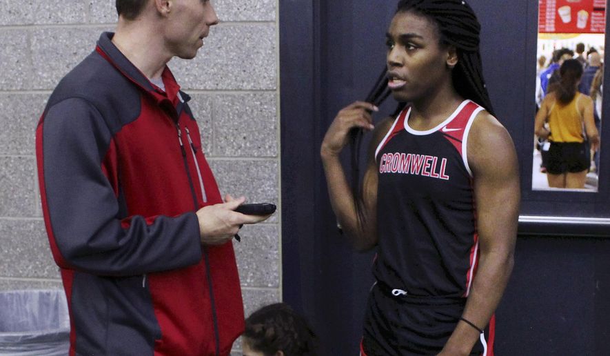 FILE — In this Feb. 7, 2019 file photo, Cromwell High School track coach Brian Calhoun, left, speaks to transgender athlete Andraya Yearwood during a break at a meet at Hillhouse High School in New Haven, Conn. Lawyers for several Connecticut school districts and the organization that oversees high school sports in the state went before a federal judge Friday, Feb. 26, 2021, seeking the dismissal of a lawsuit that would prevent transgender girls from competing in girl's sports. (AP Photo/Pat Eaton-Robb, File)