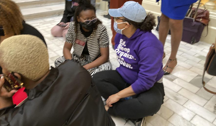 State Rep. Park Cannon, left, D-Atlanta, sits on a stairway at the Georgia state Capitol during a protest, Friday, Feb. 26, 2021, in Atlanta. Cannon and other Democrats launched the sit-in after a state trooper threatened Cannon with arrest as Democrats were protesting restrictive voting proposals. (AP Photo/Jeff Amy)