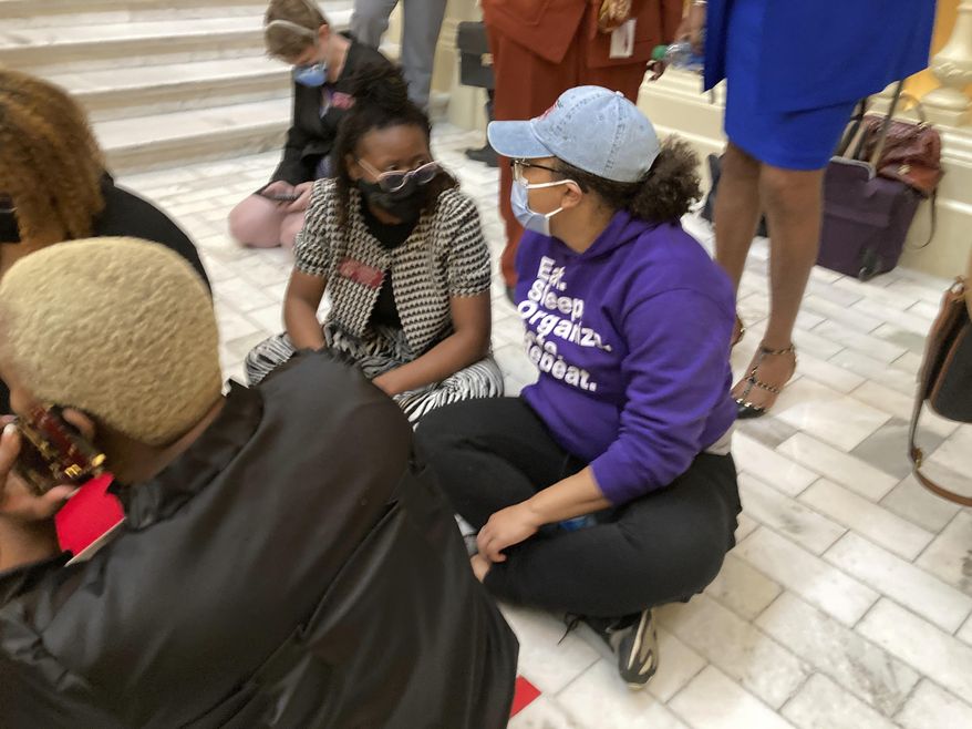 State Rep. Park Cannon, left, D-Atlanta, sits on a stairway at the Georgia state Capitol during a protest, Friday, Feb. 26, 2021, in Atlanta. Cannon and other Democrats launched the sit-in after a state trooper threatened Cannon with arrest as Democrats were protesting restrictive voting proposals. (AP Photo/Jeff Amy)