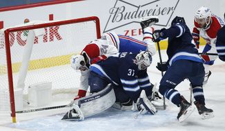 Winnipeg Jets goaltender Connor Hellebuyck (37) makes a save as Montreal Canadiens&#39; Phillip Danault (24) crashes into him during the second period of an NHL hockey game Saturday, Feb. 27, 2021, in Winnipeg, Manitoba. (John Woods/The Canadian Press via AP)
