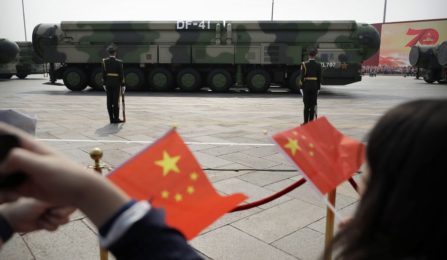 In this Oct. 1, 2019, file photo, spectators wave Chinese flags as military vehicles carrying DF-41 ballistic missiles roll during a parade to commemorate the 70th anniversary of the founding of Communist China in Beijing. (AP Photo/Mark Schiefelbein) ** FILE **