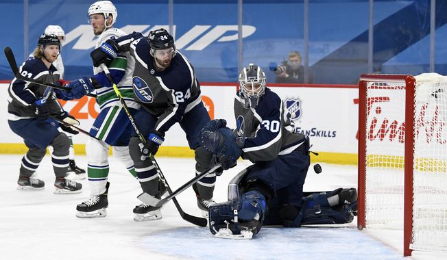 Winnipeg Jets goaltender Laurent Brossoit (30) looks back as a shot by Vancouver Canucks&#x27; Elias Pettersson (not shown) gets by him for a goal during the first period of an NHL game in Winnipeg, Manitoba, on Tuesday, March 2, 2021. (Fred Greenslade/The Canadian Press via AP)