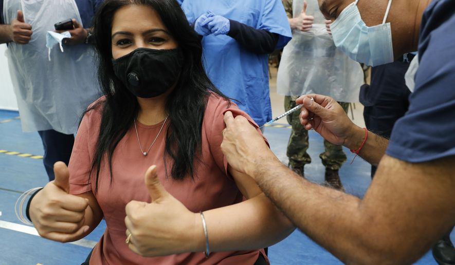 Doctor Anil Mehta, surrounded by his team of doctors, administers a dose of the Pfizer vaccine to Geeta Waddon to mark the 10,000th jab in his small practice in London, Sunday, Feb. 28, 2021. (AP Photo/Frank Augstein)