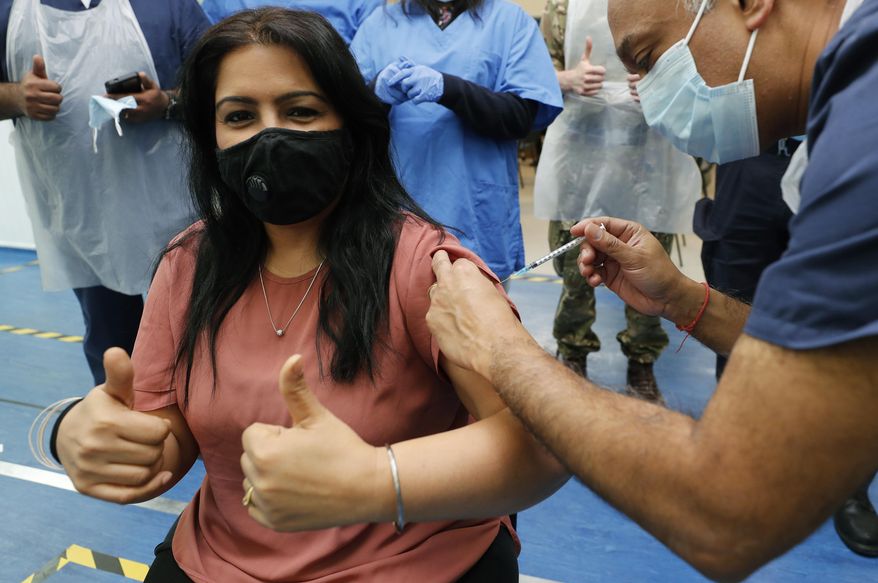 Doctor Anil Mehta, surrounded by his team of doctors, administers a dose of the Pfizer vaccine to Geeta Waddon to mark the 10,000th jab in his small practice in London, Sunday, Feb. 28, 2021. (AP Photo/Frank Augstein)