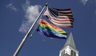 In this Friday, April 19, 2019 file photo, a gay pride rainbow flag flies with the U.S. flag in front of the Asbury United Methodist Church in Prairie Village, Kan.  (AP Photo/Charlie Riedel)  **FILE**