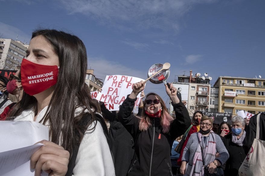 A woman bangs together kitchen utensils as she participates in a rally to ask for more respect for women's rights, in the Kosovo capital Pristina on Monday, March 8, 2021, marking International Women's Day. Participants held banners, hit kitchen utensils causing cracking sounds, to protest against the home violence which is a main complaint in a patriarchal society with hundreds of cases registered at police every year. (AP Photo/Visar Kryeziu)