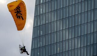 An activist of environmental organization Greenpeace flies with a motorized paraglider past the European Central Bank in Frankfurt, Germany, Wednesday, March 10, 2021. Two activists landed on the roof of a side building and unrolled a banner to protest against the ECB&#39;s climate policy. (AP Photo/Michael Probst)
