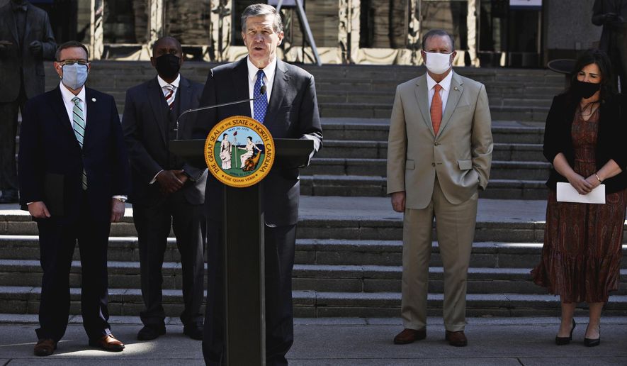 North Carolina Gov. Roy Cooper, center, and lawmakers gather Wednesday, March 10, 2021, for a news conference to announce that leaders of the Republican-led state legislature and the governor have reached an agreement to reopen the state&#x27;s K-12 public schools to full-time daily instruction in Raleigh.  (Juli Leonard/The News &amp;amp; Observer via AP)