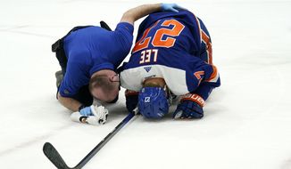 A trainer tends to New York Islanders left wing Anders Lee (27), who had collided with a New Jersey Devils player during the first period of an NHL hockey game Thursday, March 11, 2021, in Uniondale, N.Y. Lee left the game. (AP Photo/Kathy Willens)
