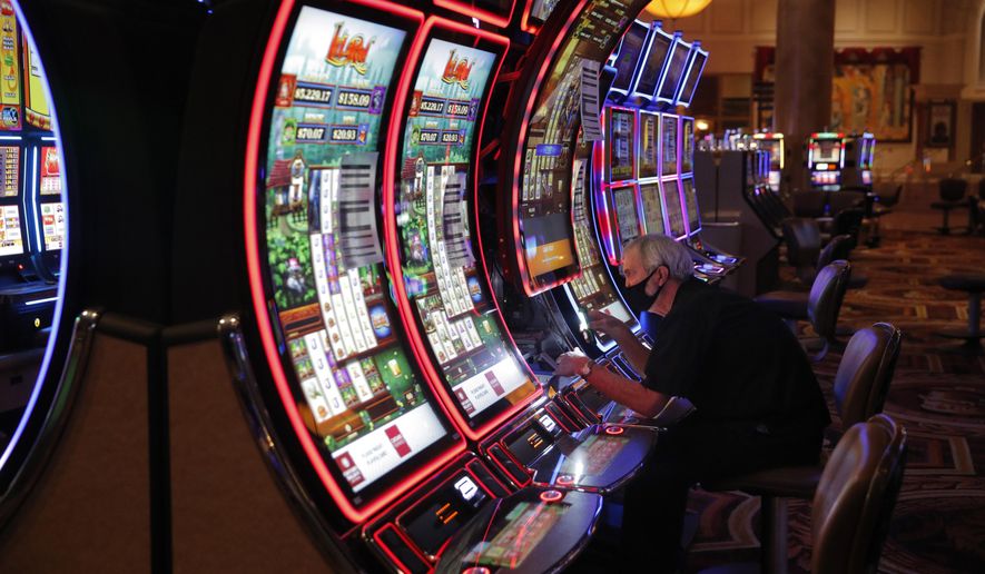 FILE - In this May 21, 2020, file photo, a worker works on an electronic slot machine as chairs have been removed from some machines to maintain social distancing between players at a closed Caesars Palace hotel and casino in Las Vegas. Workers in the key Las Vegas restaurant, hospitality and casino industry can now get a coronavirus vaccine. State COVID-19 response officials issued a statement Thursday, March 11, 2021, immediately adding "Frontline Commerce and Service Industries" in Clark County to the eligibility list. (AP Photo/John Locher, File)