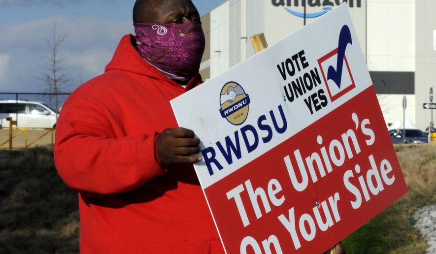 In this Tuesday, Feb. 9, 2021 file photo ,Michael Foster of the Retail, Wholesale and Department Store Union holds a sign outside an Amazon facility where labor is trying to organize workers in Bessemer, Ala. (AP Photo/Jay Reeves, File)  **FILE**
