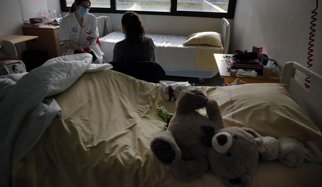 Psychiatrist Coline Stordeur speaks with a young girl in her room in the pediatric unit of the Robert Debre hospital, in Paris, France, Tuesday, March 2, 2021. Doctors say the impact of the coronavirus pandemic on the mental health of children is alarming and plain to see. (AP Photo/Christophe Ena)