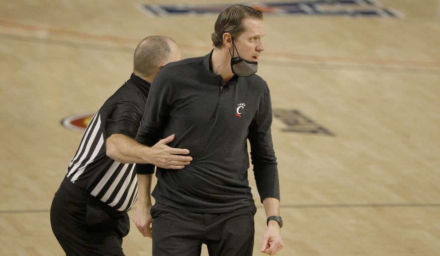 Cincinnati head coach John Brannen is pulled back toward the team bench by a game official as Cincinnati plays Wichita State during the second half of an NCAA college basketball game in the semifinal round of the American Athletic Conference men's tournament Saturday, March 13, 2021, in Fort Worth, Texas. (AP Photo/Ron Jenkins)
