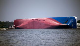 FILE - In this Sept. 9, 2019, file photo, a Moran tugboat nears the stern of the capsizing vessel Golden Ray near St. Simons Sound off the coast of Georgia. Demolition of the large cargo ship along the coast of Georgia is entering its fifth month, with work to chop the ship into eight large pieces going far slower than the salvage crew anticipated. (AP Photo/Stephen B. Morton, File)